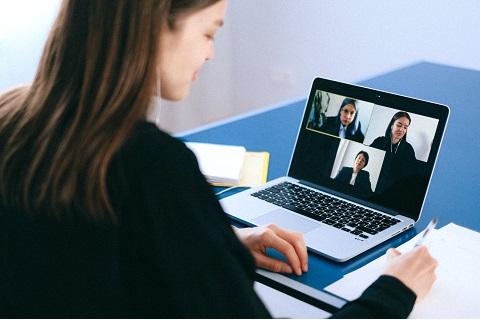 Obraz przedstawia dziewczynę która bierze udział w spotkaniu online, przed sobą ma komputer na którym widnieją trzy osoby ( dwie młodsze kobiety i jedna starsza)